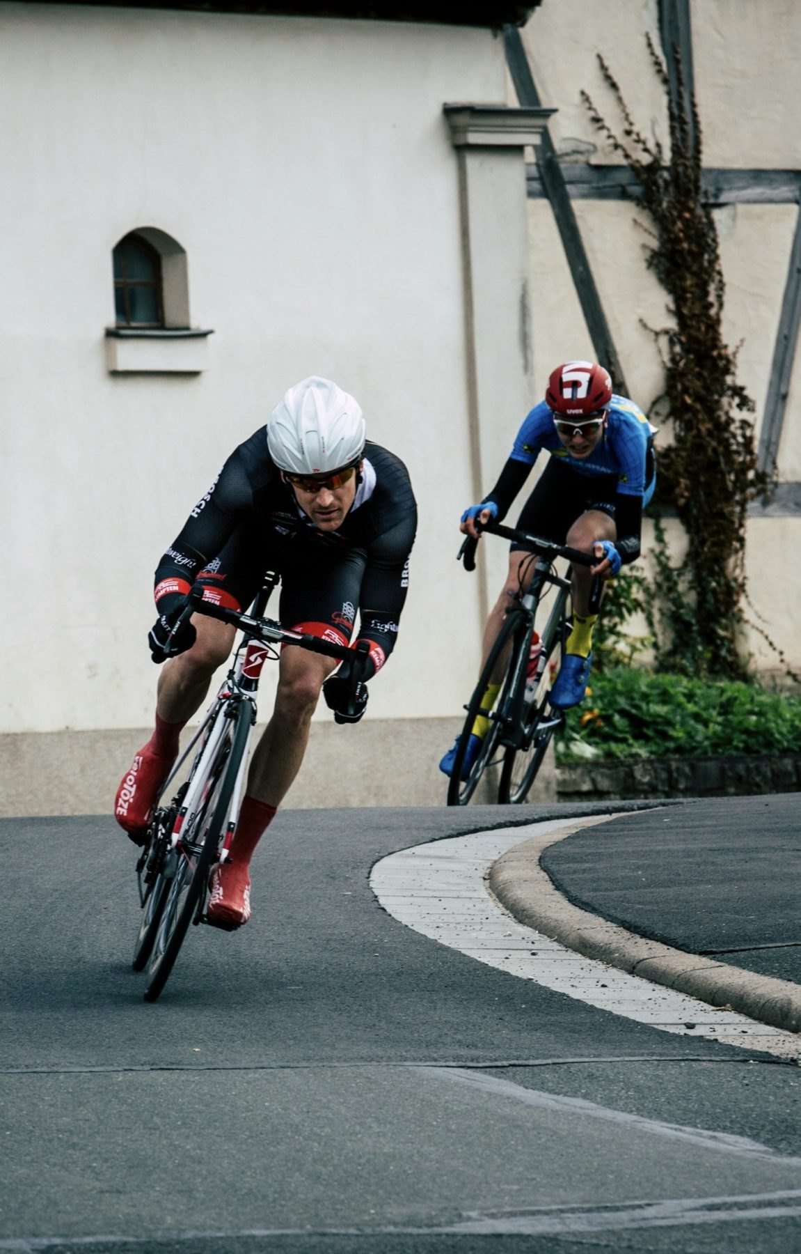 Twee wielrenners die achter elkaar aan fietsen door een Duitse plaats.