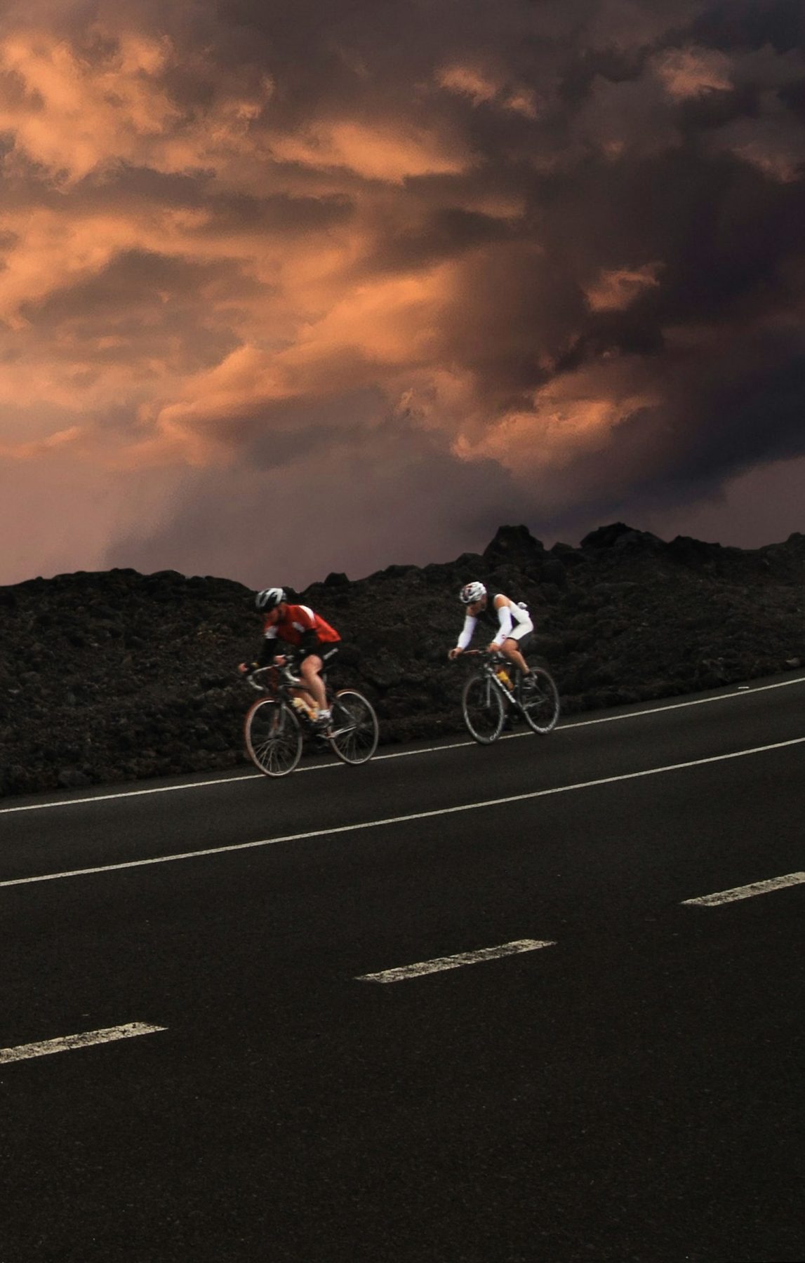 Twee mensen fietsend over een weg in Lanzarote in Spanje met donkere wolken op de achtergrond.