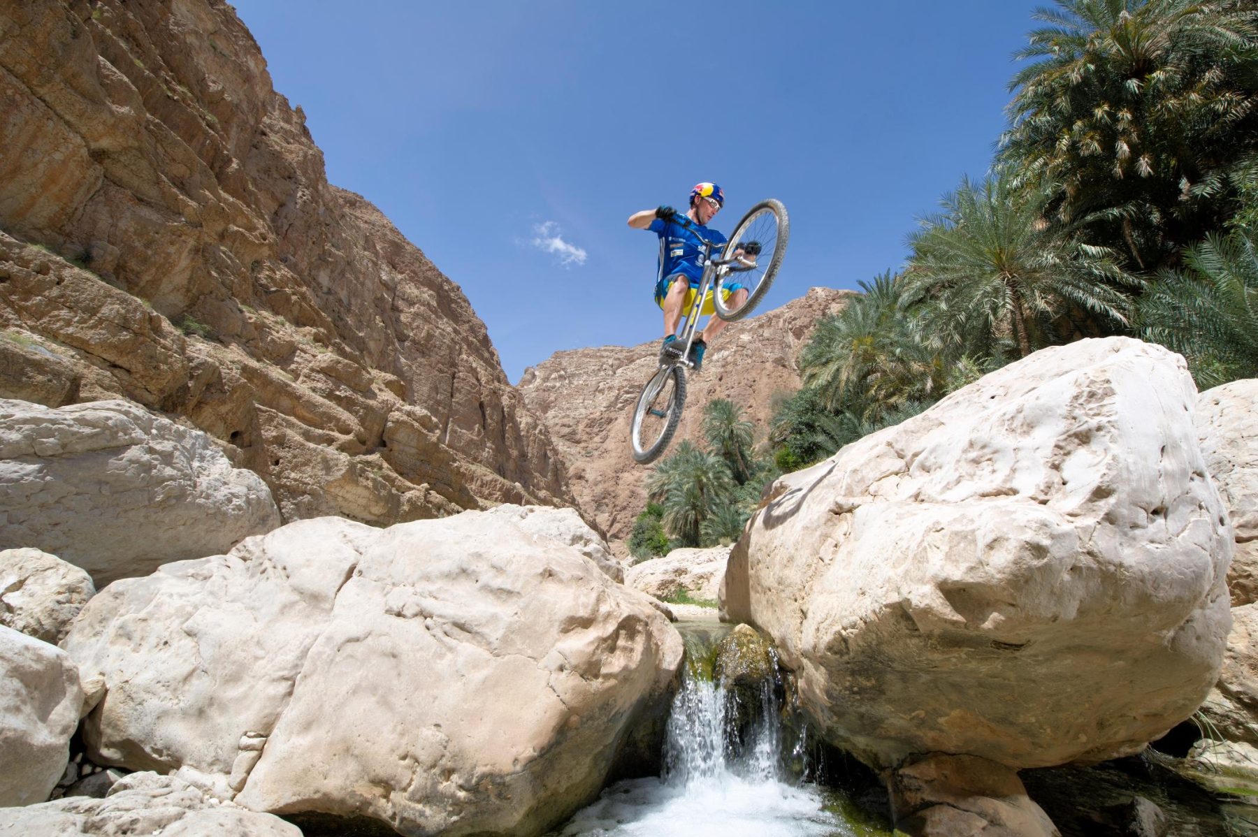 Een man doet een truc op een mountainbike over verschillende grote stenen in Oman.