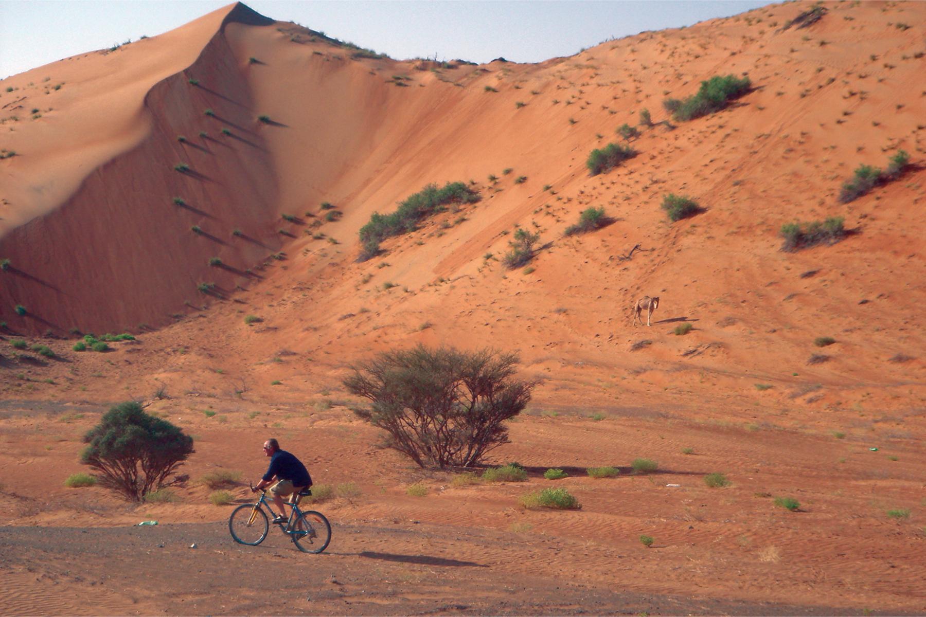 Een man fietsend door de woestijn in Oman.